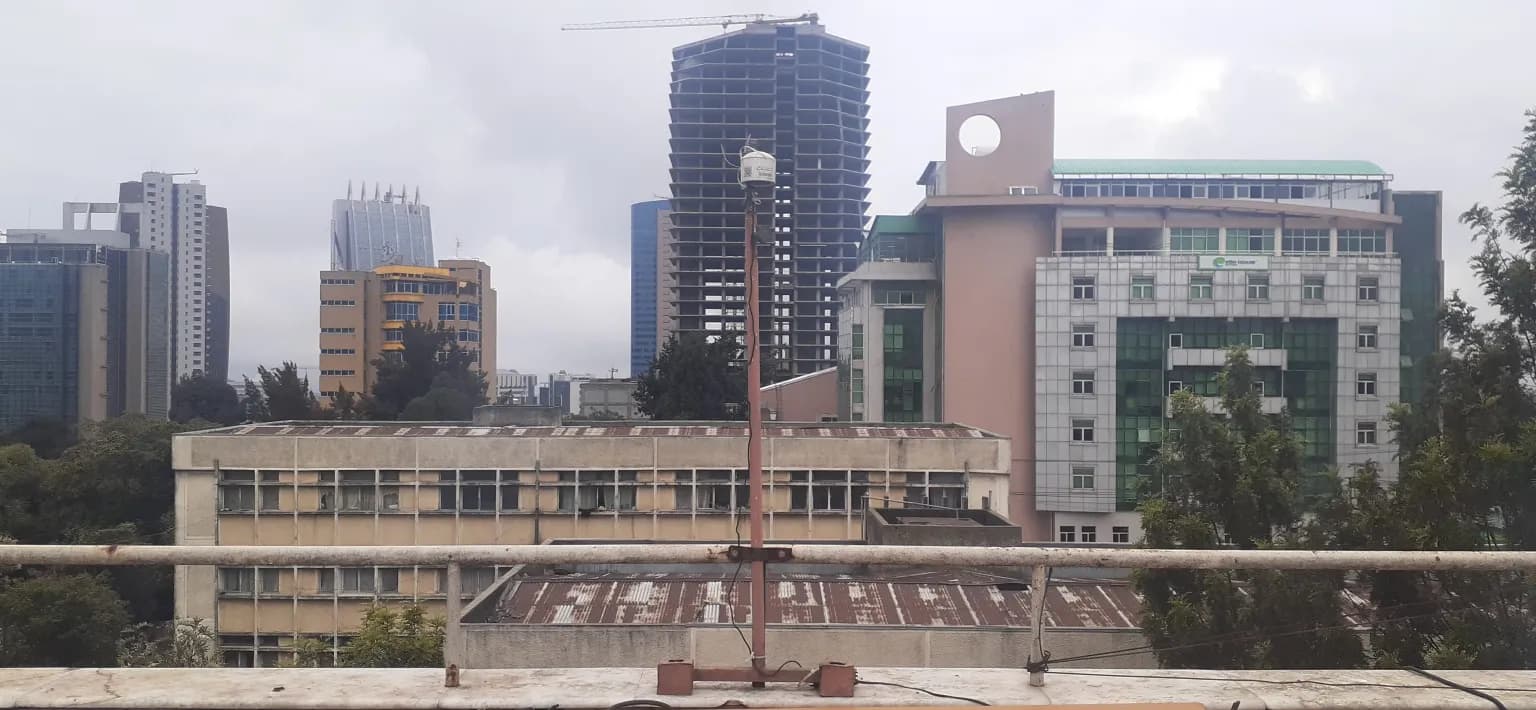 A roof-mounted air-quality sensor above central Addis Ababa with city buildings behind it