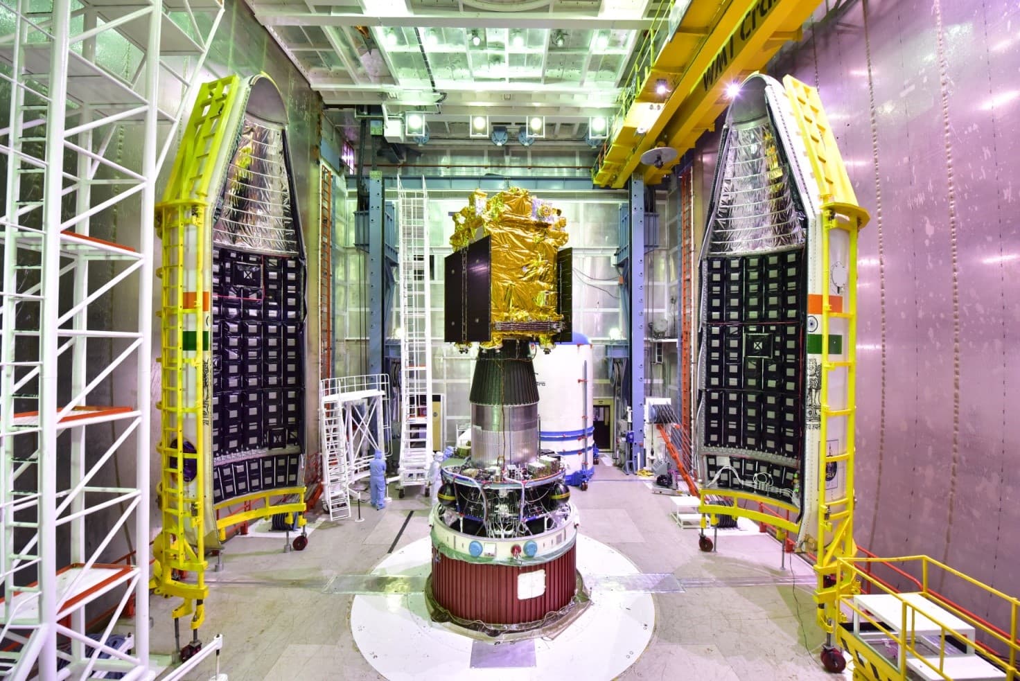 Gold-covered Aditya-L1 spacecraft mounted on its rocket stage between two open payload-fairing halves in an integration building