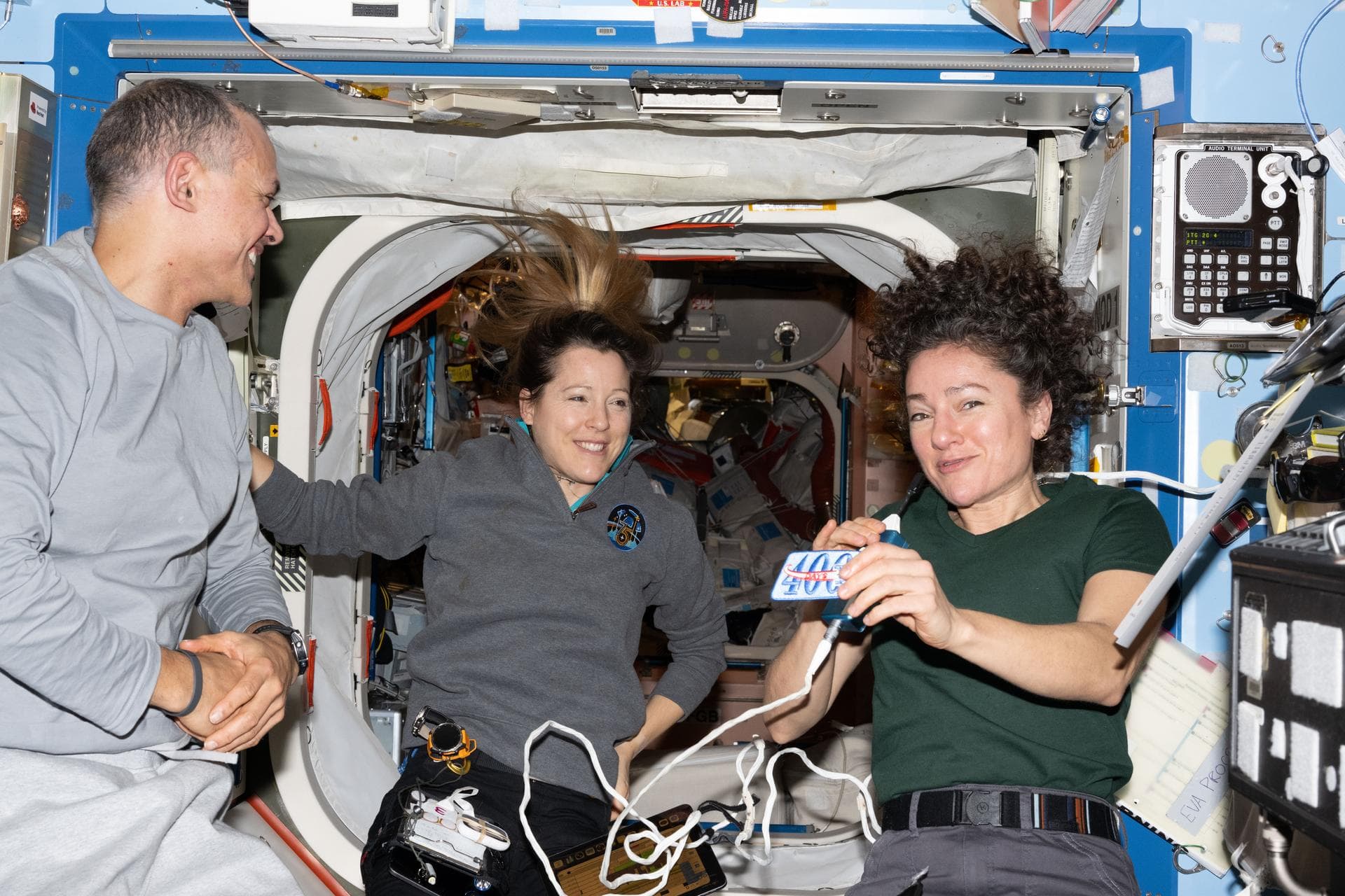 Anil Menon at left with Sophie Adenot and Jessica Meir, who holds a commemorative patch inside the space station