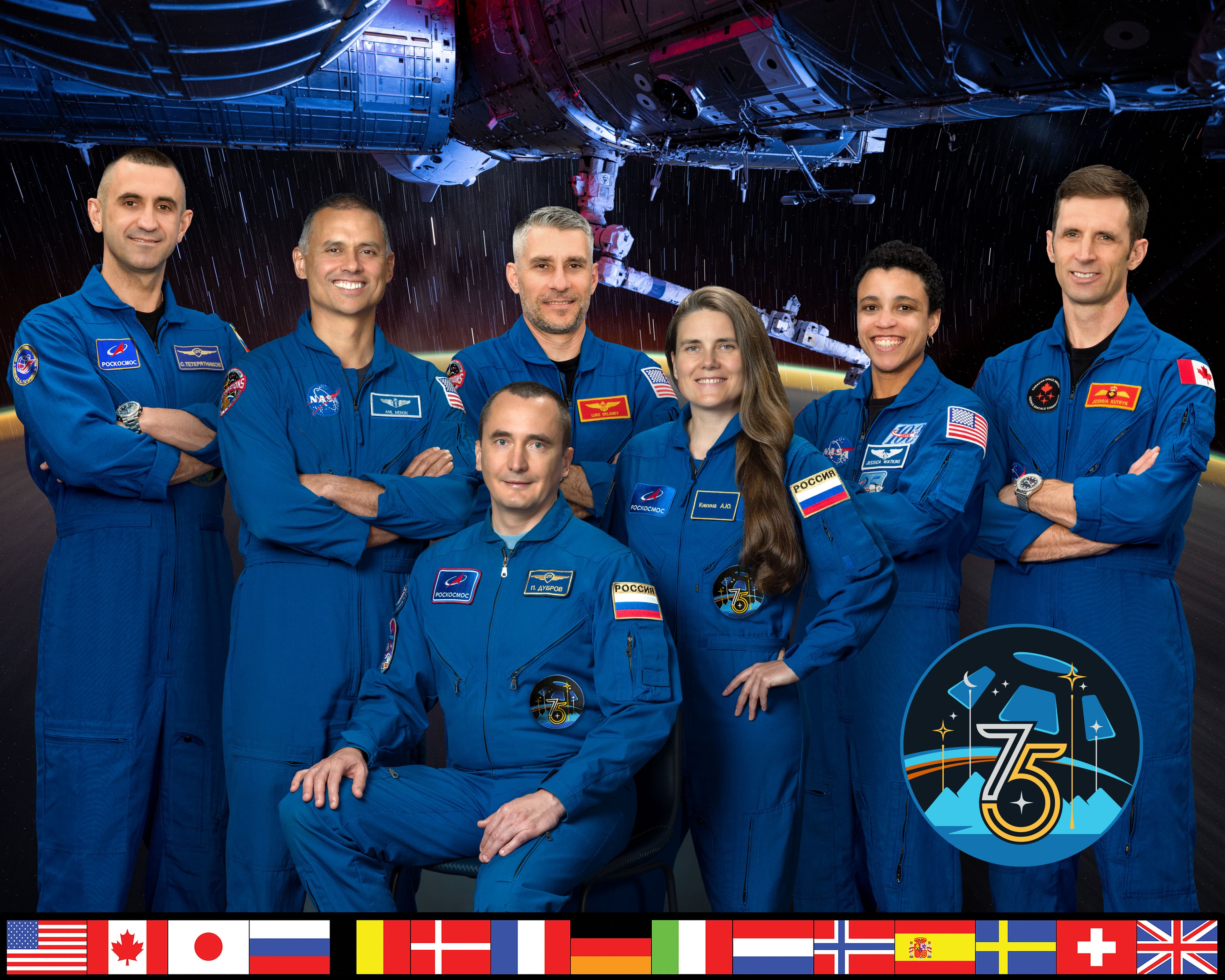 Seven Expedition 75 crew members in blue flight suits, with Anil Menon second from left