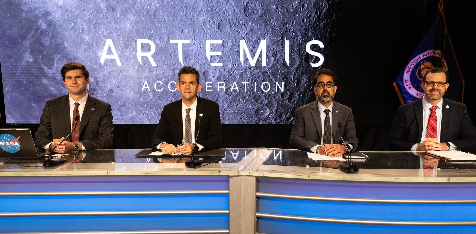 Four NASA officials sit at a desk with microphones beneath an Artemis Acceleration backdrop.