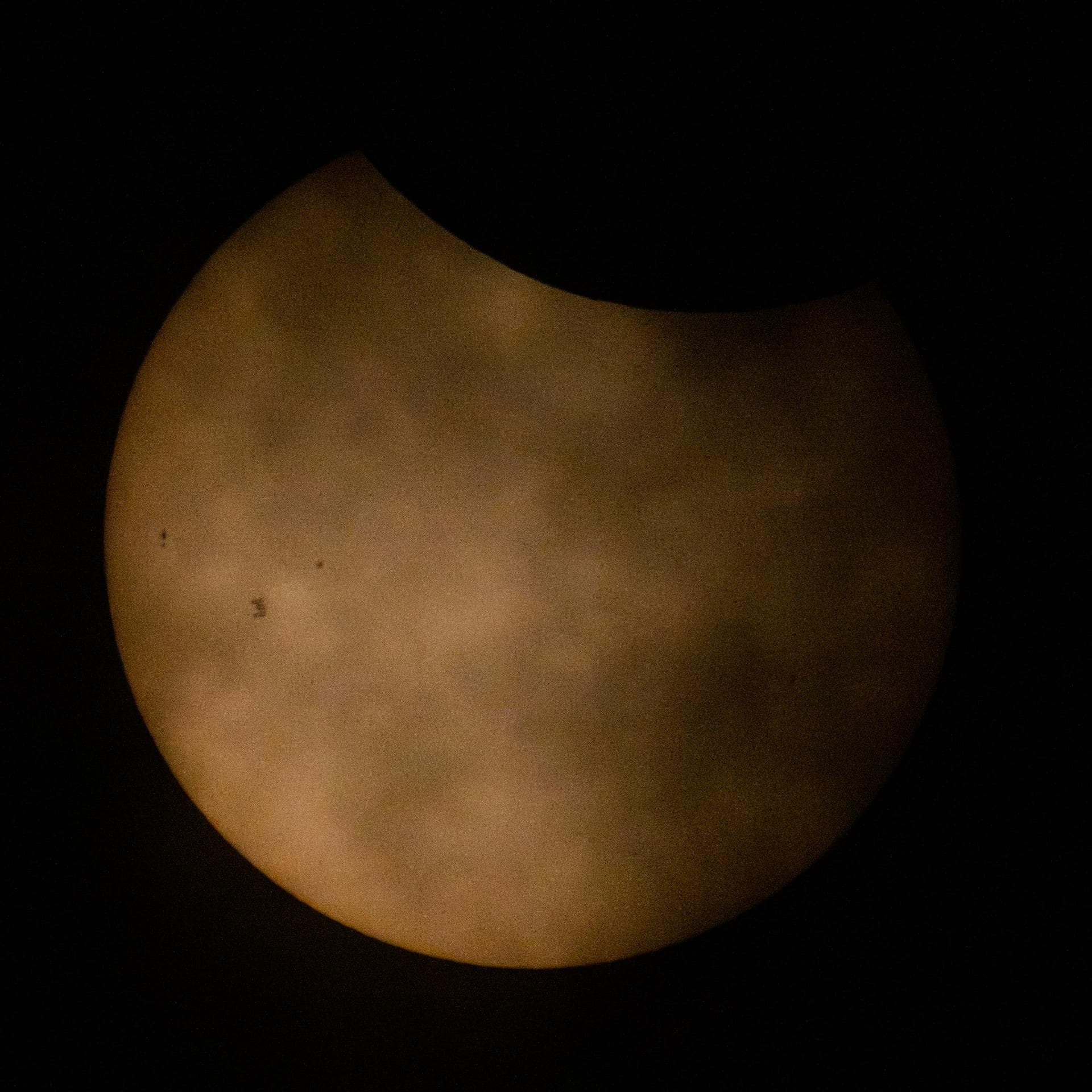 International Space Station silhouetted against a partially eclipsed Sun behind thin clouds