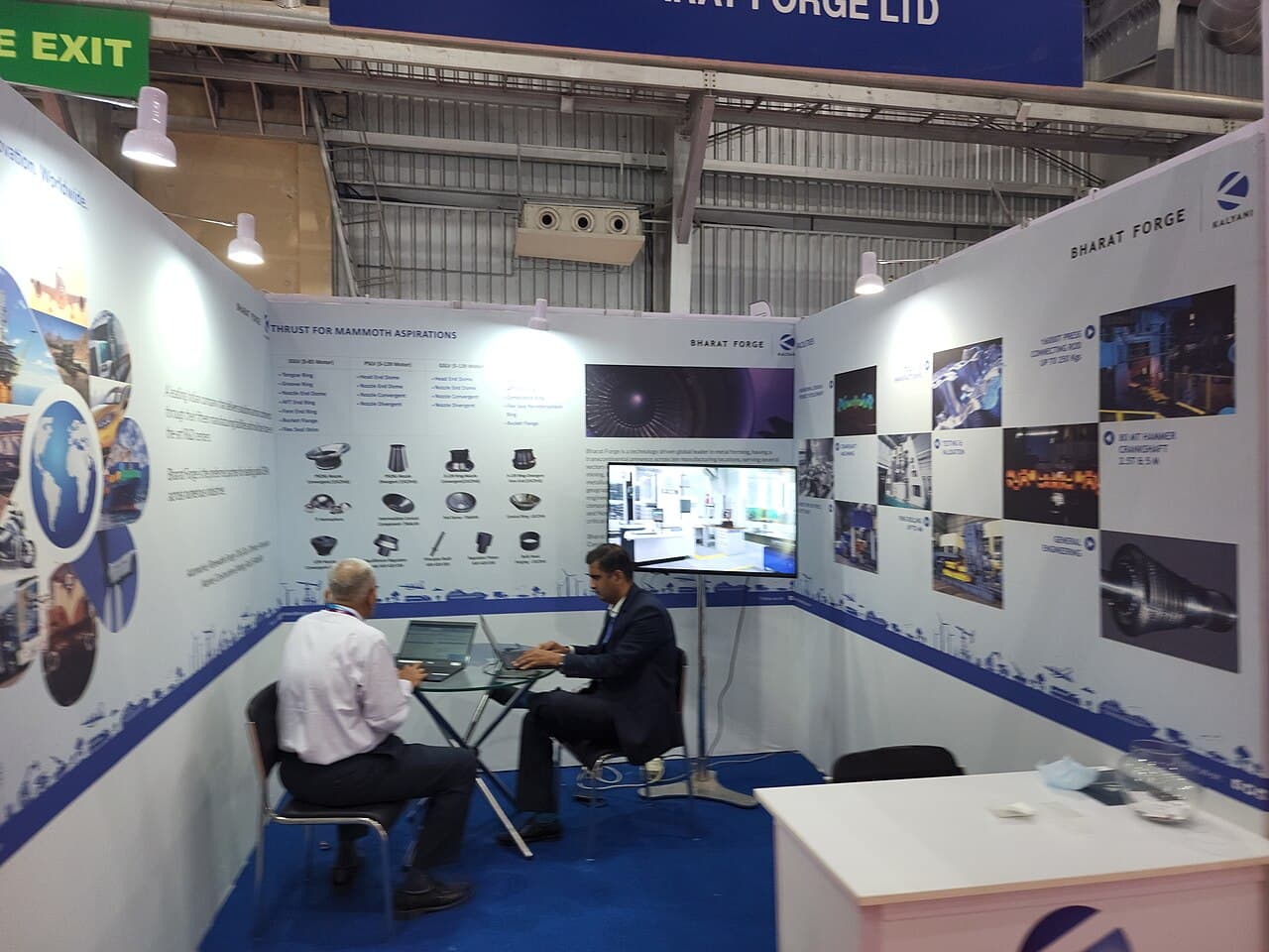 Bharat Forge exhibition stall with component displays and two visitors seated at a table
