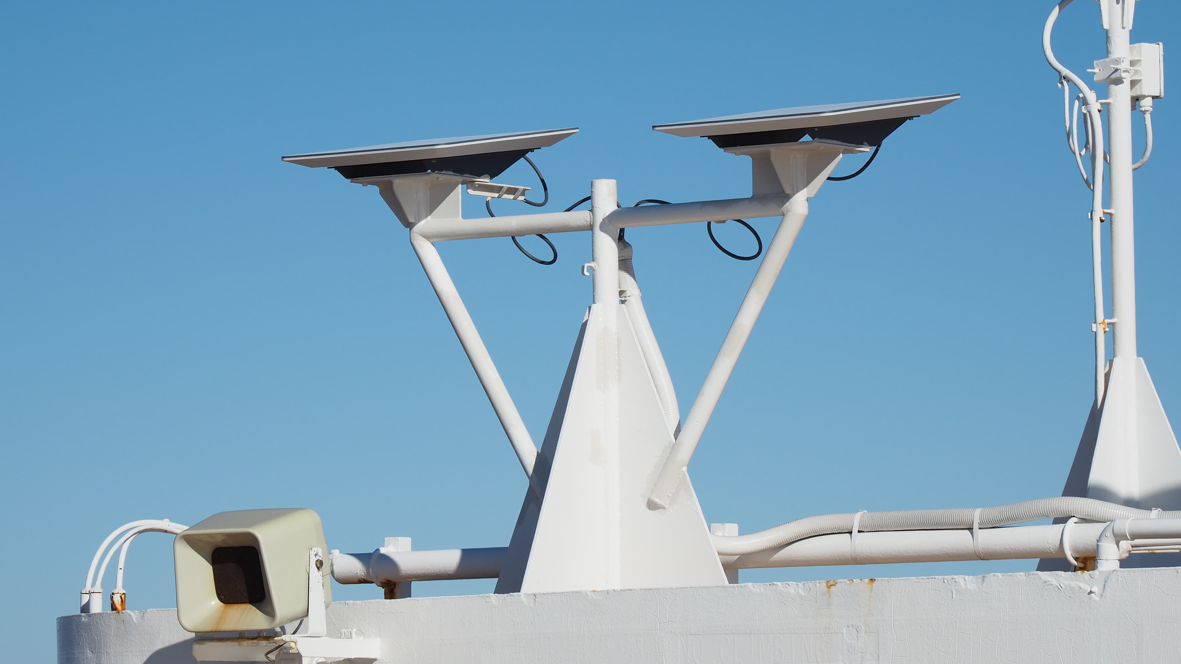 Two flat Starlink antennas mounted on white supports aboard a ship beneath a clear blue sky