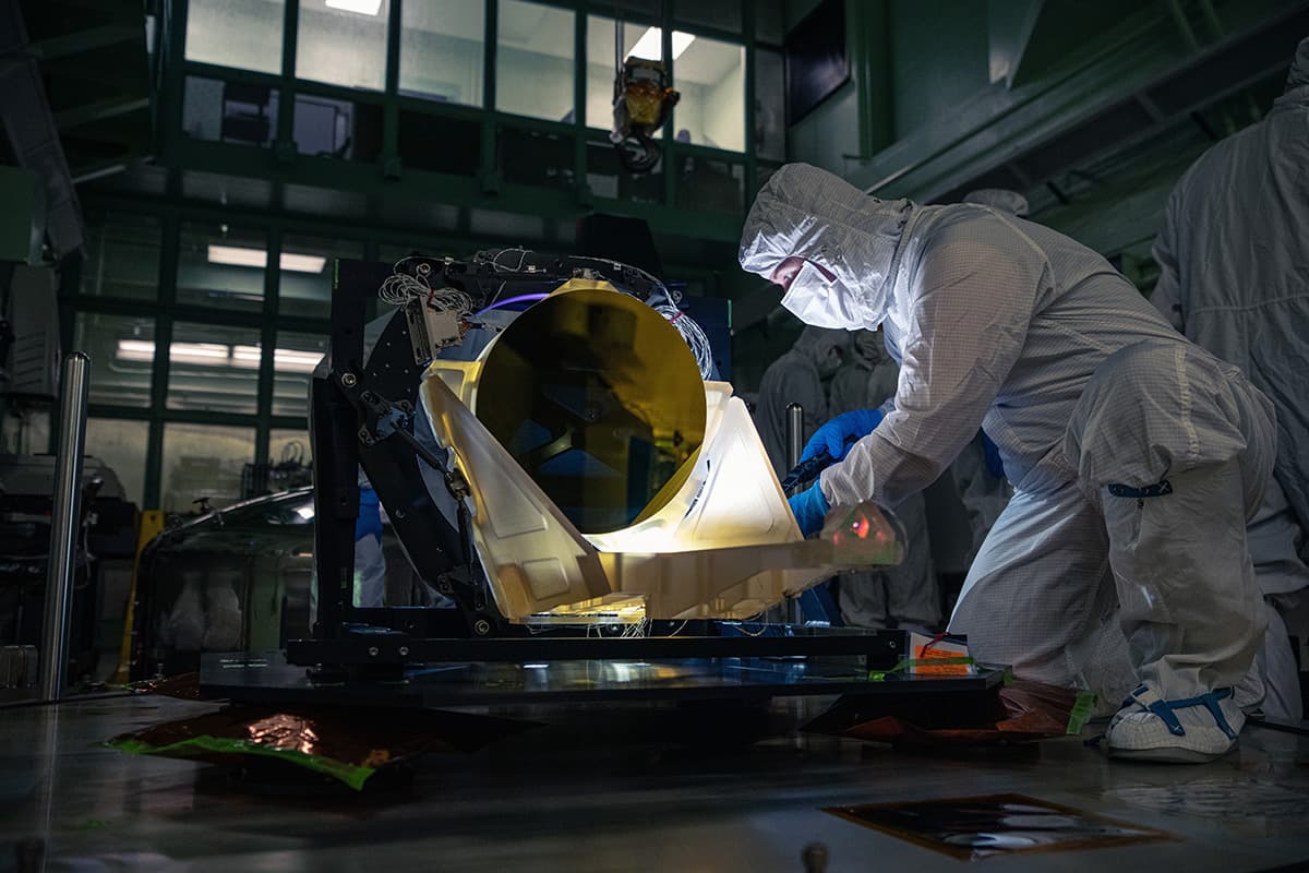 A technician in clean-room clothing inspects a gold-coated LISA prototype telescope at NASA Goddard