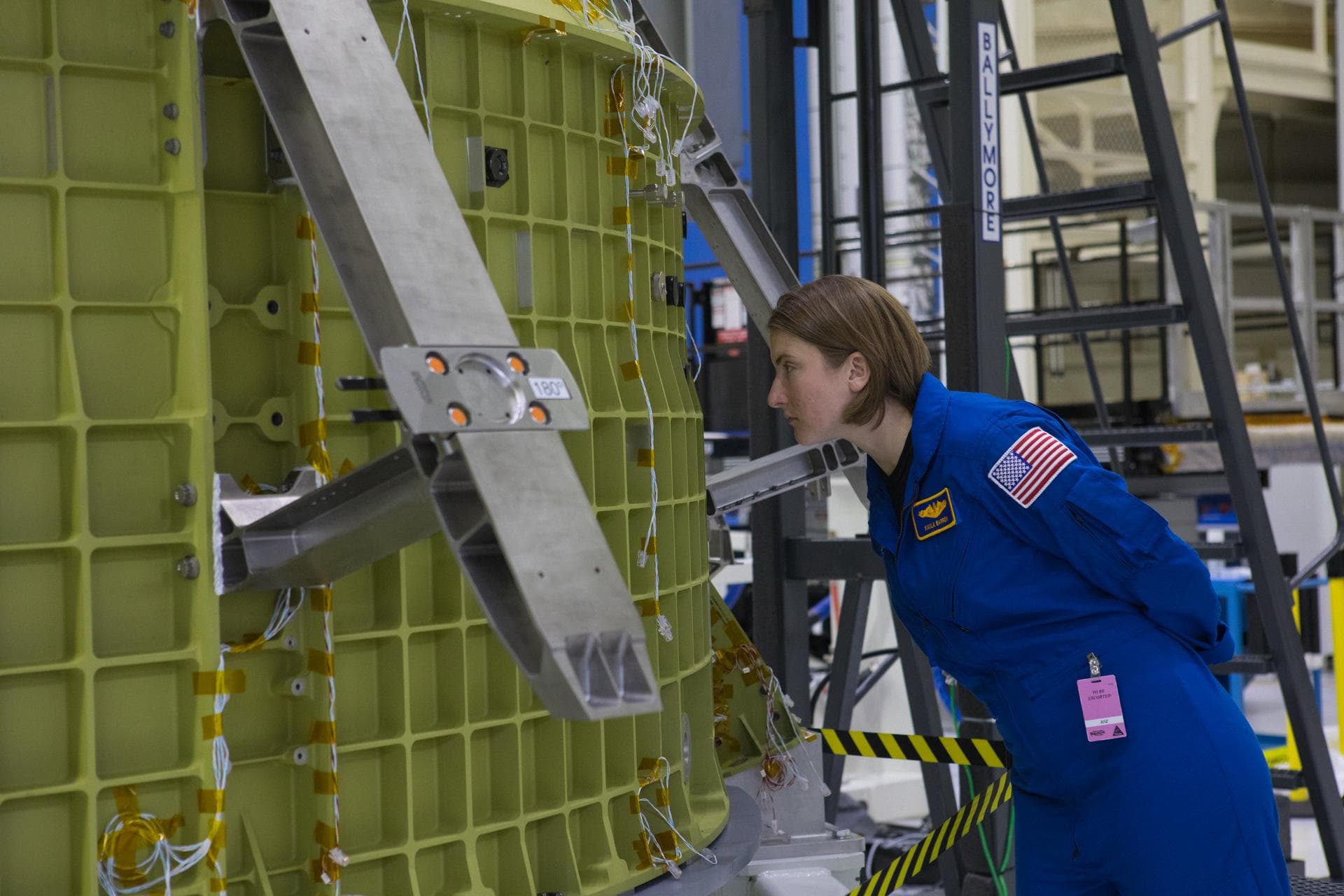 Kayla Barron in a blue NASA flight suit viewing the Orion pressure vessel inside Kennedy Space Center