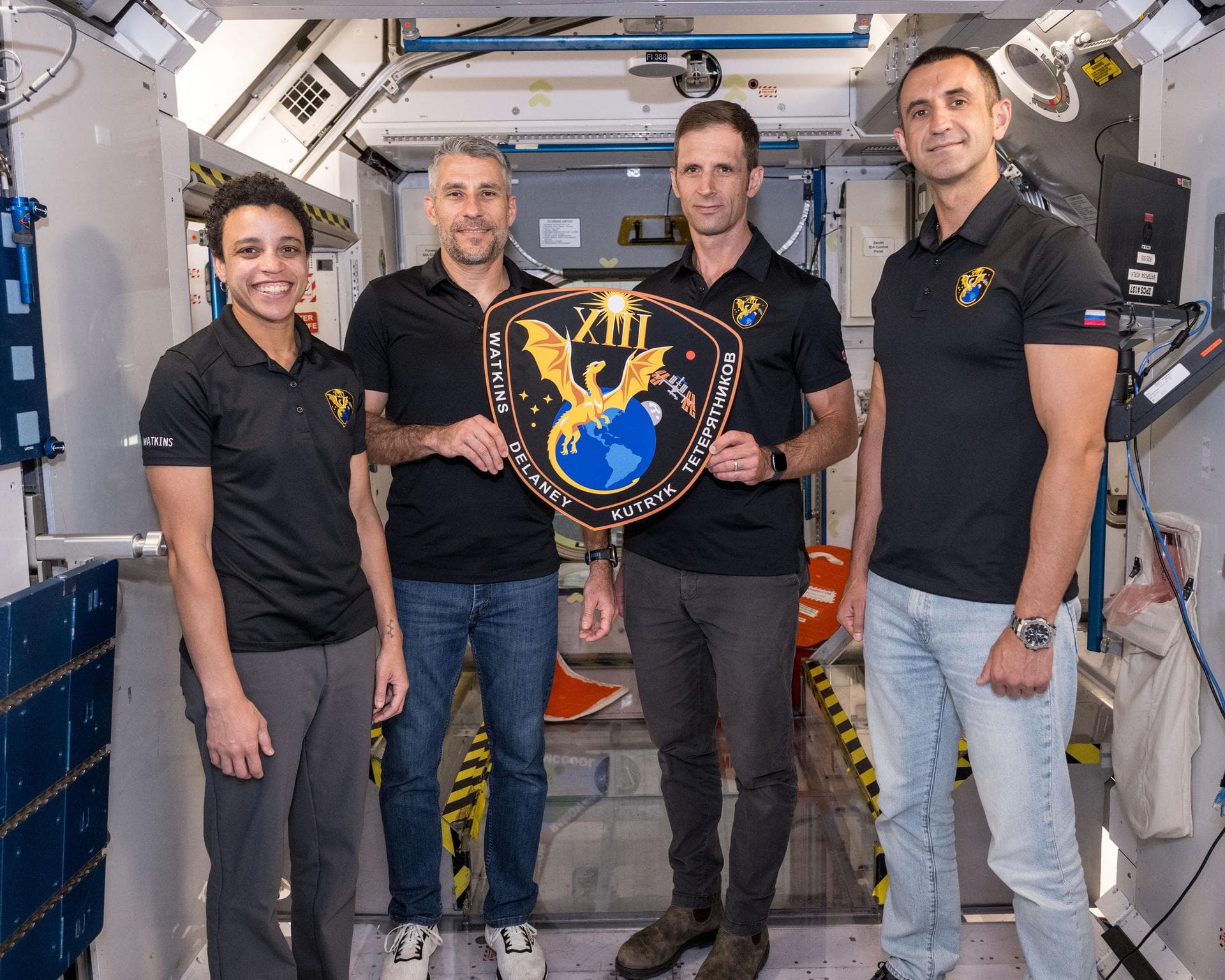 The four Crew-13 astronauts hold their mission plaque inside a space-station training mockup