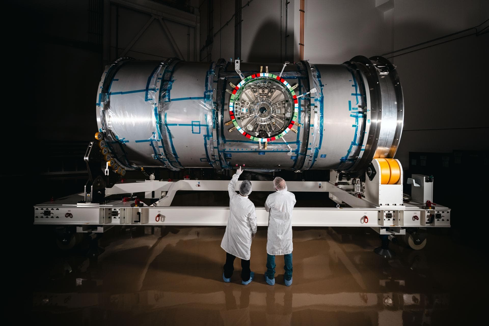 Two technicians in cleanroom clothing inspect the cylindrical HALO module at a Northrop Grumman facility