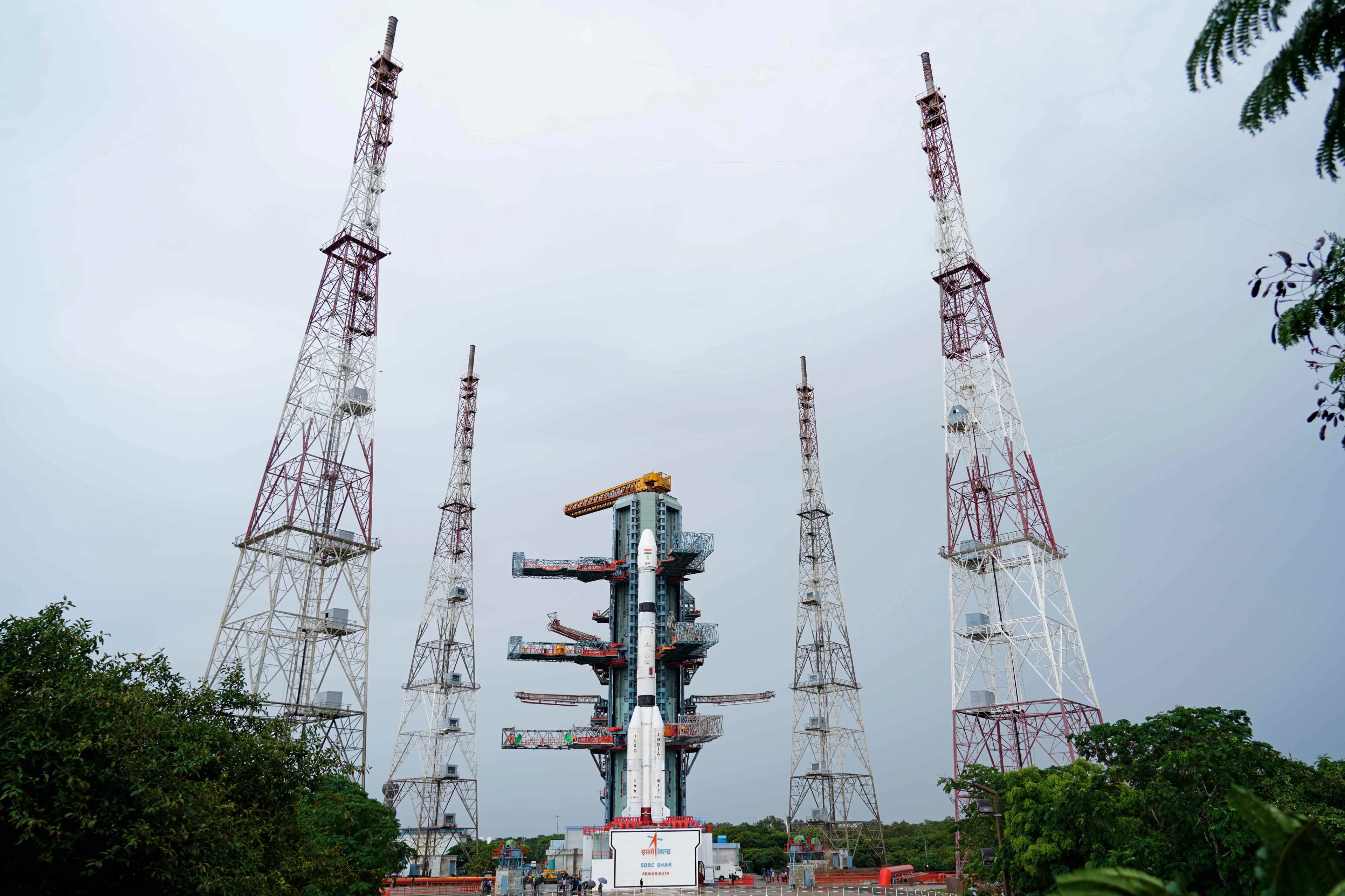 GSLV-F18 rocket beside its launch tower, surrounded by four tall lightning-protection towers