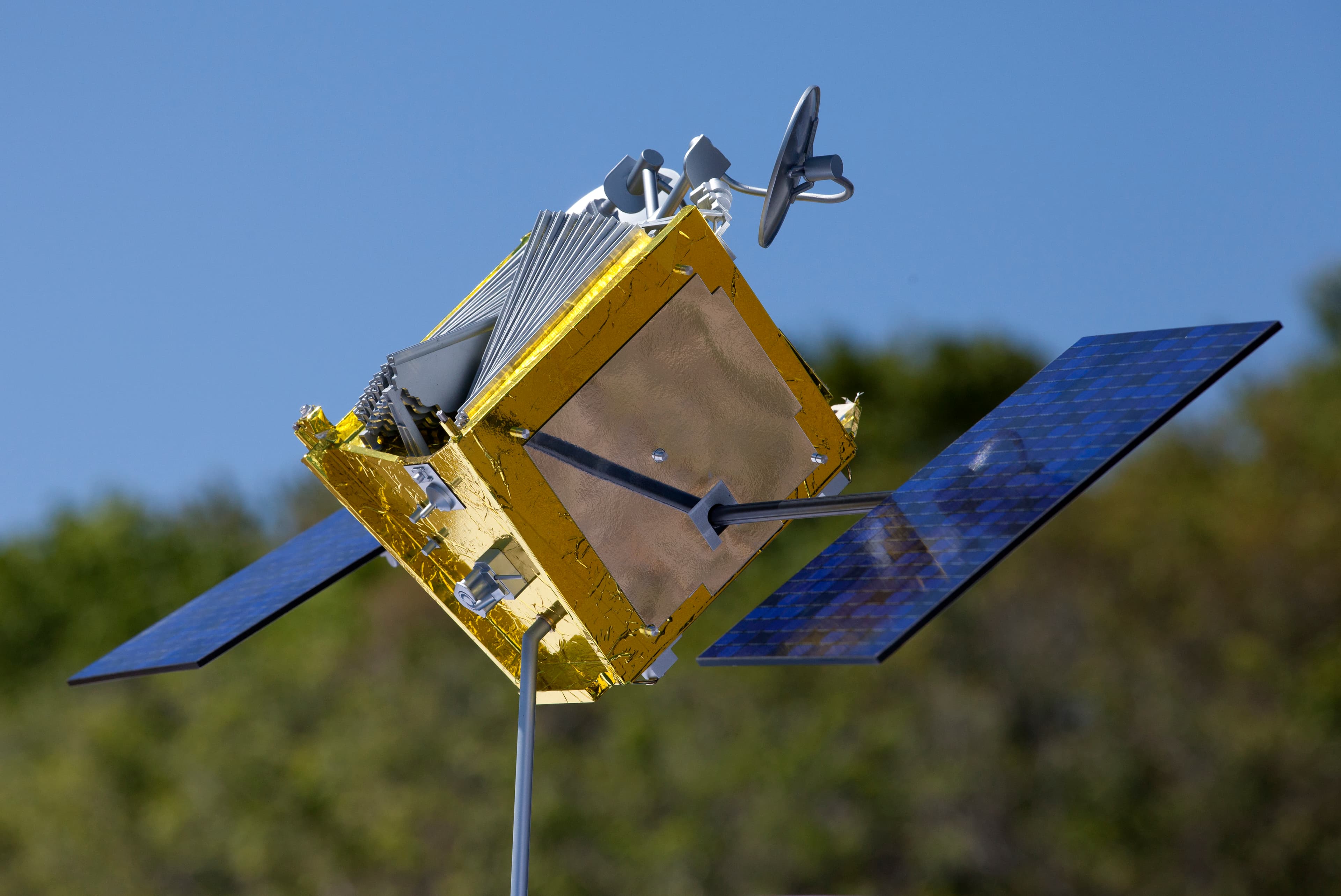 A gold-coloured OneWeb satellite model with antennas and blue solar panels on a stand outdoors