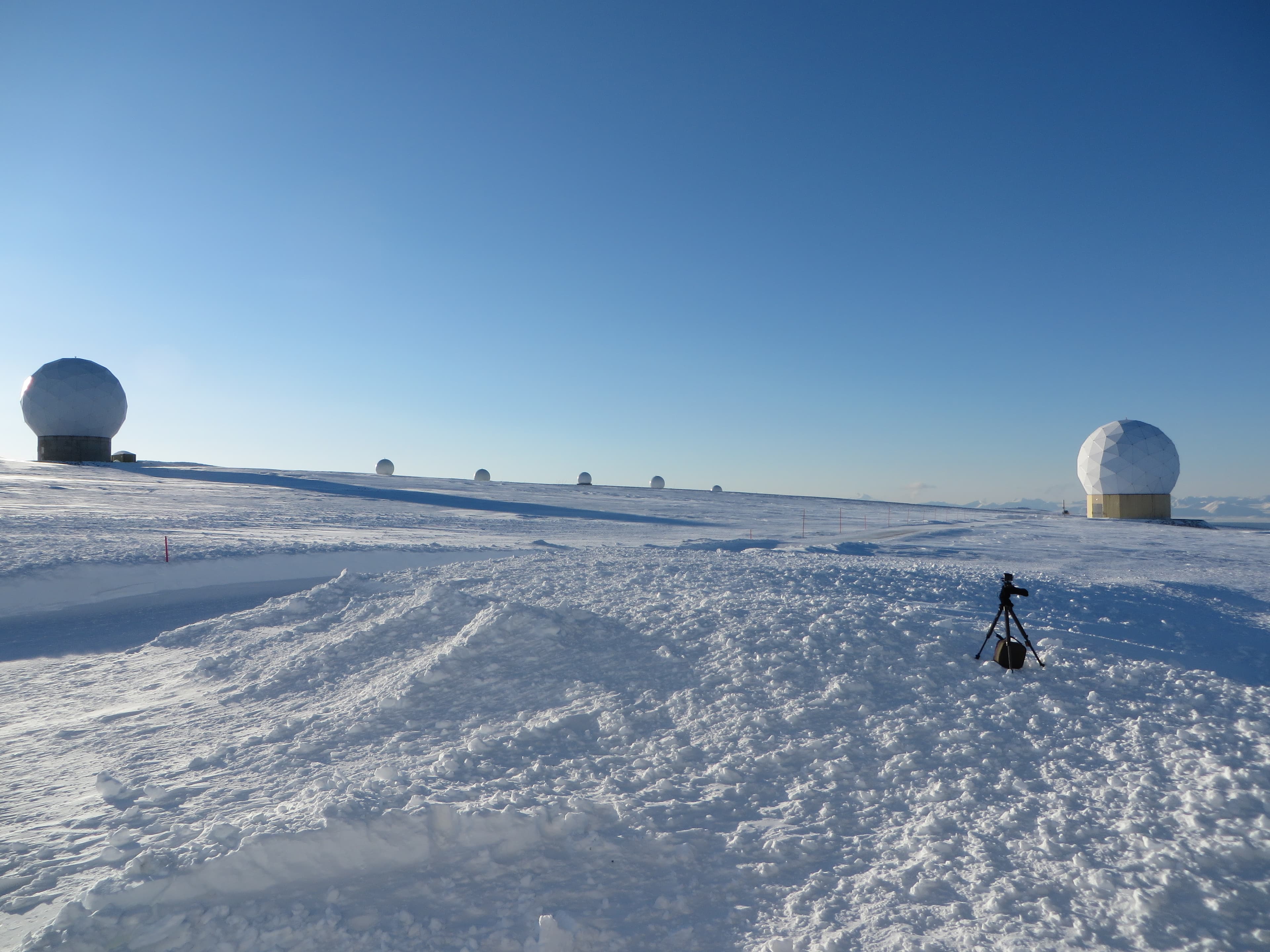 White antenna radomes across a snow-covered plateau under a clear blue sky at SvalSat