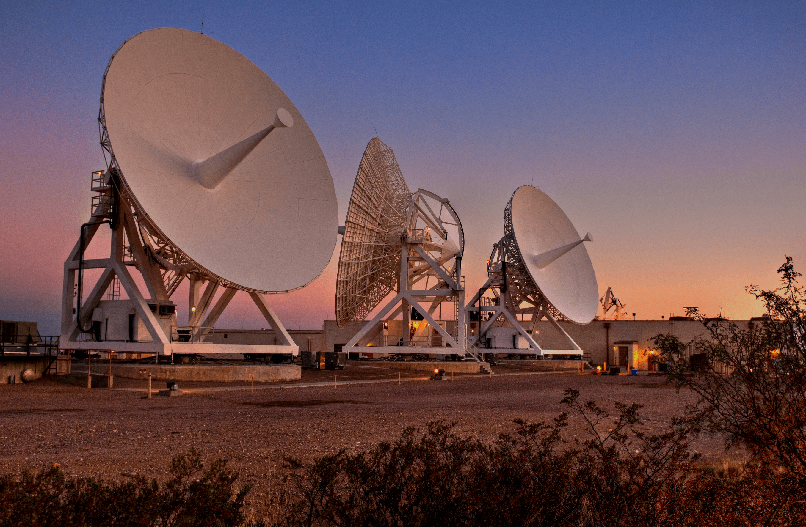 Three large radio antennas at White Sands, New Mexico, under a pink and blue sunset sky