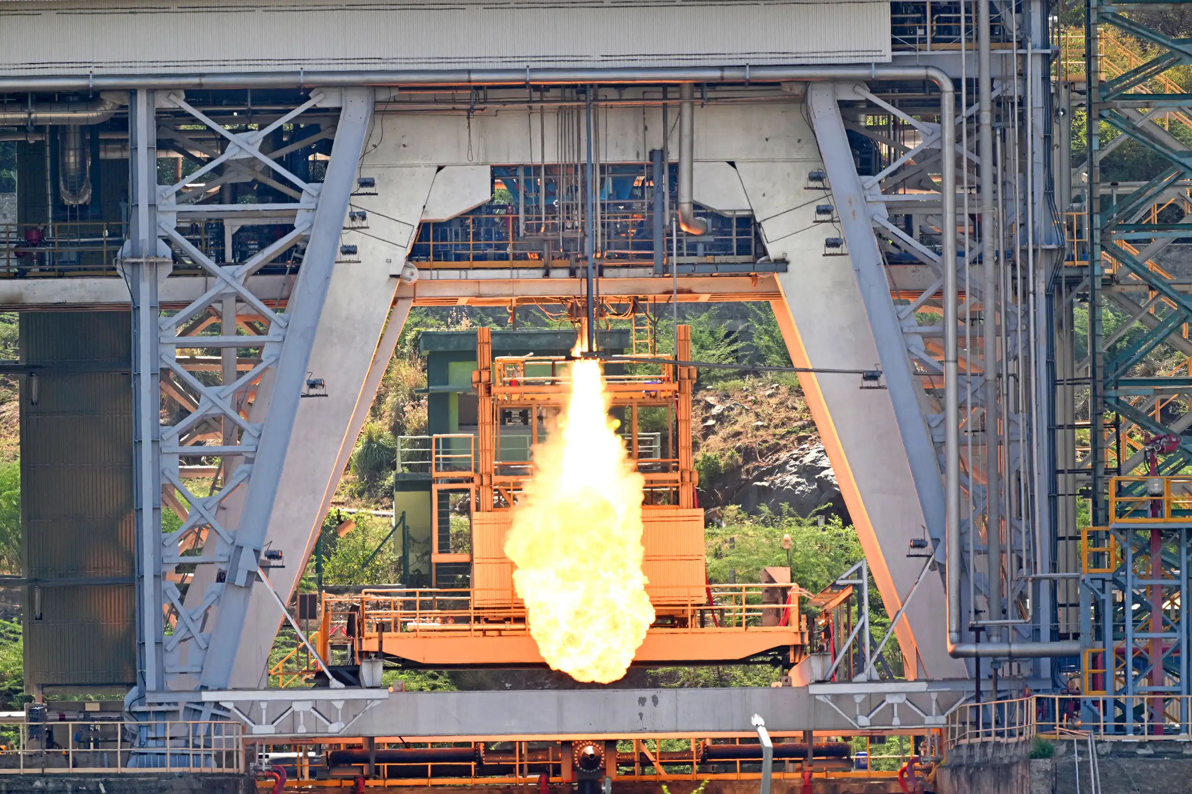 A bright engine exhaust plume fires beneath a semi-cryogenic power-head test article inside a steel test stand
