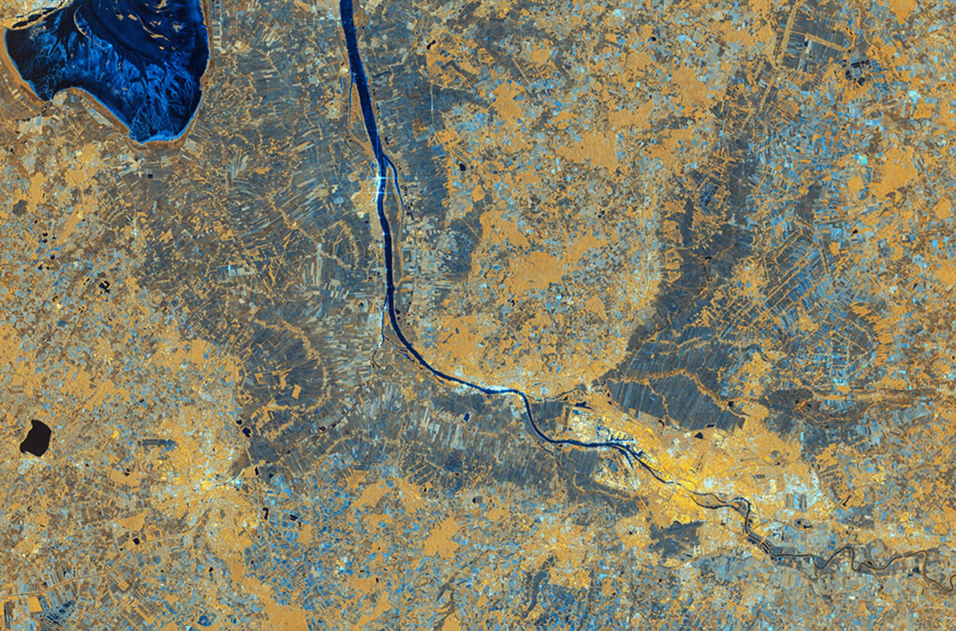 False-colour radar image of Bremen, with a dark blue winding river and gold and blue urban and agricultural patterns