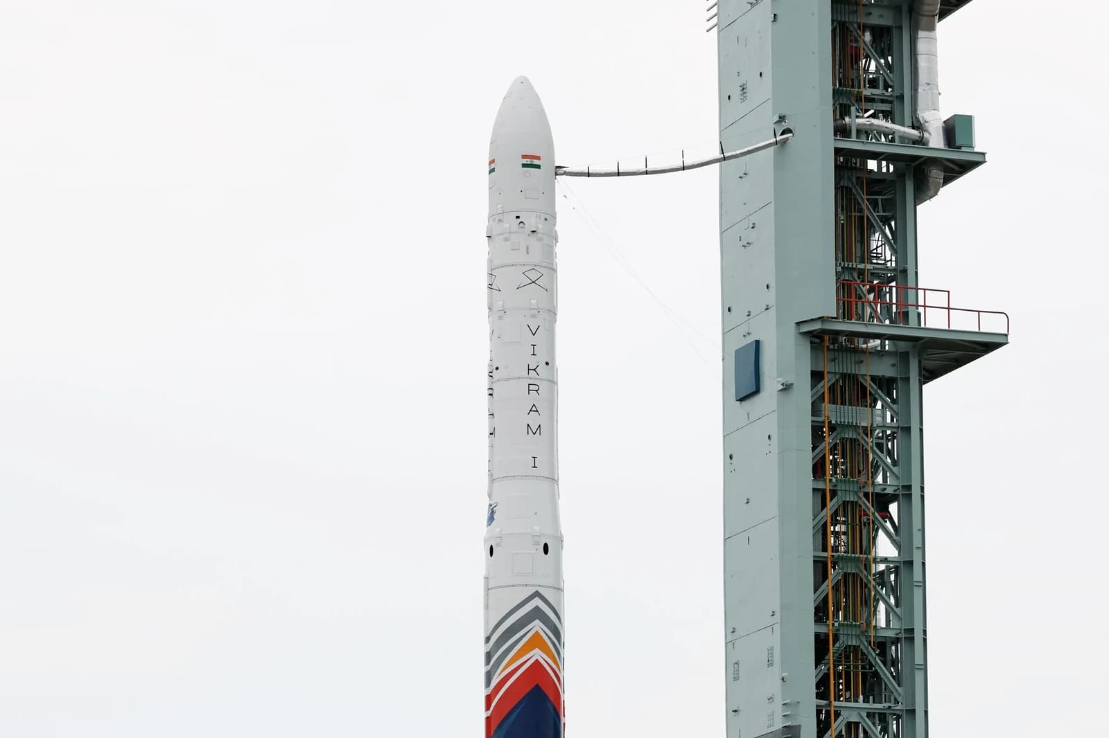 Upper section of a Vikram-1 rocket beside its launch tower under an overcast sky