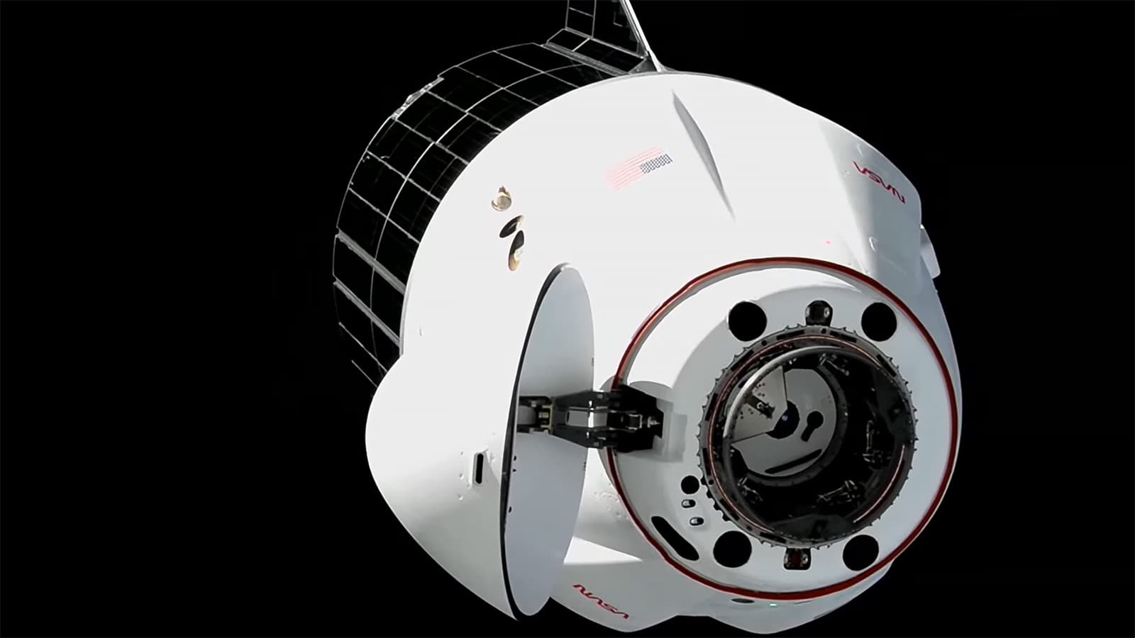 Cargo Dragon with its nose cone open approaches the station against black space