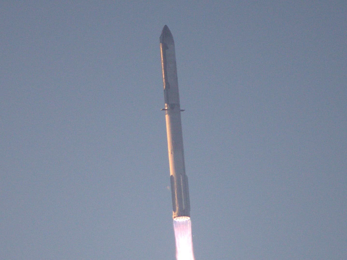 Starship and its Super Heavy booster climbing through the sky with a bright engine plume shortly after liftoff