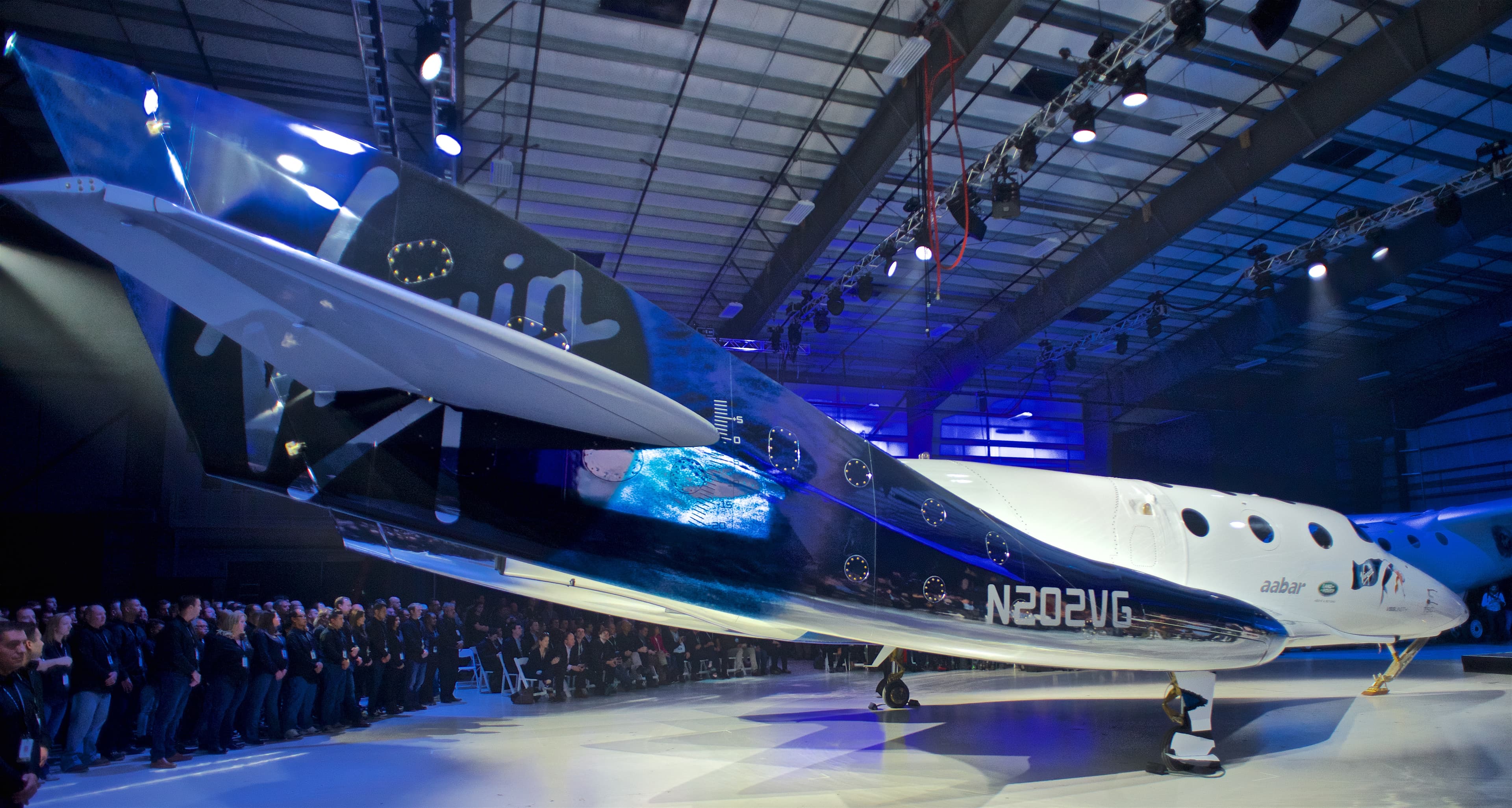 VSS Unity spaceplane inside a hangar at its rollout, with spectators standing behind it