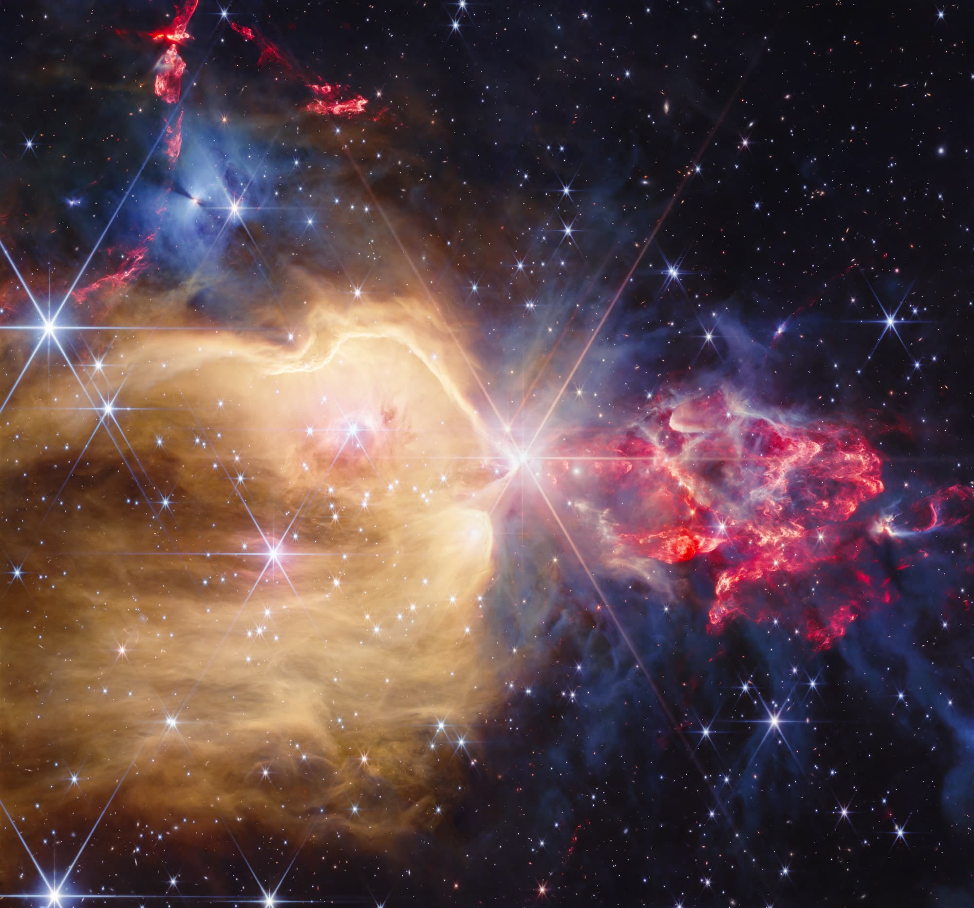 Infrared composite of a star cluster with a golden gas cavity on the left, red clumpy outflows on the right and blue nebulosity above
